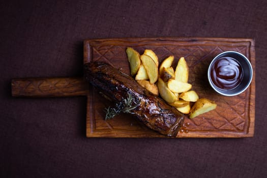 A juicy and tender beef steak is served with crispy potato wedges and a side of rosemary on a wooden board.