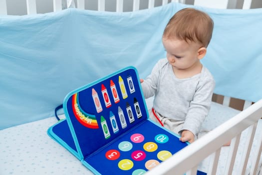 One year old baby sitting in a crib playing with montessori busy book