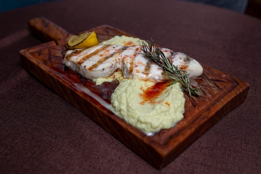 A delicious and healthy meal of grilled fish fillet with lemon and herb butter, served on a wooden board.