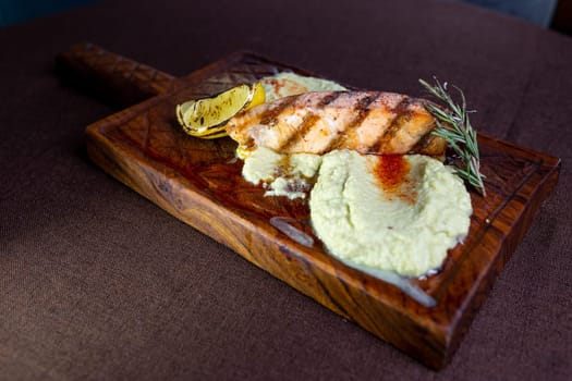 A mouthwatering grilled salmon fillet topped with a zesty lemon-herb butter sauce, presented elegantly on a rustic wooden serving board.