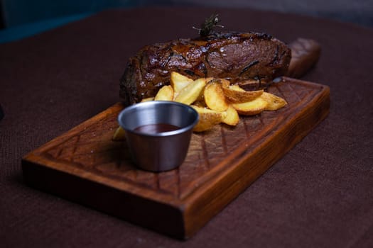 A juicy and tender beef steak is served with crispy potato wedges and a side of rosemary on a wooden board.