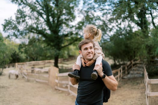 Dad with a little girl on his shoulders stands in the park and looks away. High quality photo