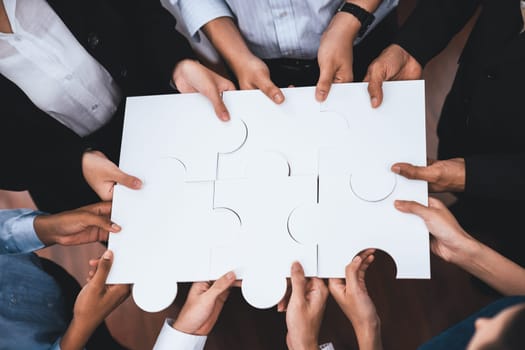 Diverse corporate officer workers collaborate in office, connecting puzzle pieces to represent partnership and teamwork. Unity and synergy in business concept by merging jigsaw puzzle. Concord