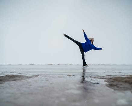 Caucasian woman in a blue sweater is skating on a frozen lake. Figure skater performs a swallow