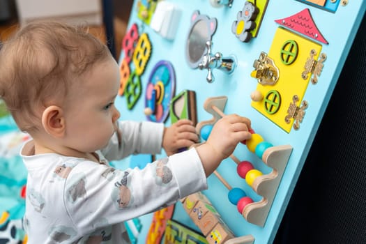 Profile of a cute baby playing with wooden elements on a busy board.