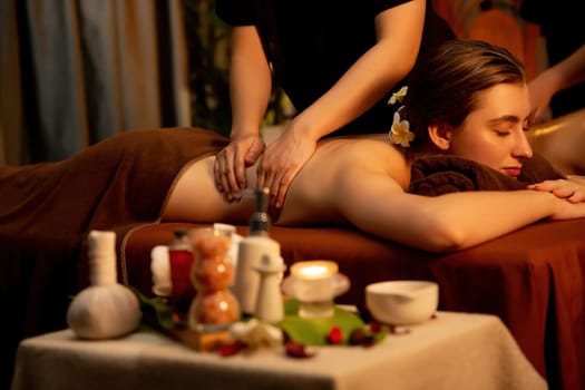 Caucasian couple customer enjoying relaxing anti-stress spa massage and pampering with beauty skin recreation leisure in warm candle lighting ambient salon spa at luxury resort or hotel. Quiescent