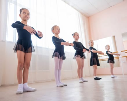 Cute little girls in black swimsuits and tutu practice ballet in class