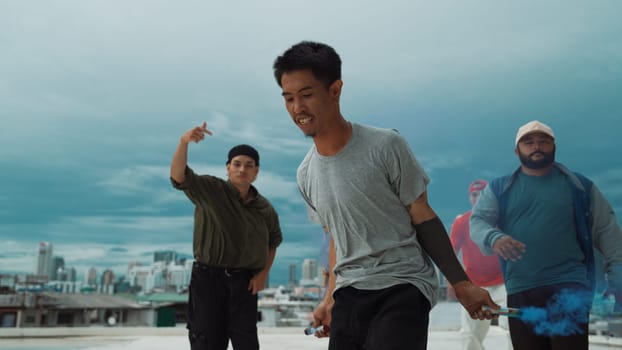 Group of multicultural hipster playing color flare at rooftop. Attractive street dancer holding colored smoke and perform break dance move to hip-hop music. Outdoor sport 2024. Endeavor.