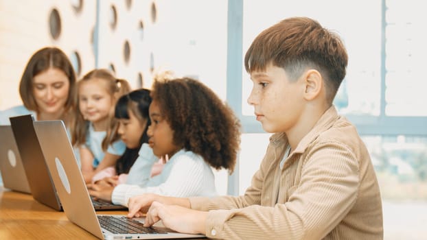 Boy playing laptop with multicultural friend learning prompt at STEM technology class. Multicultural student study about engineering code and programing system with blurring background. Erudition.