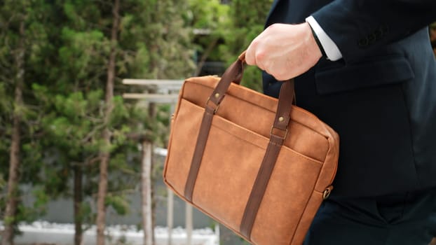 Close up of suitcase was held by profession businessman while project manager walking up stairs or step to new position at green eco city. Happy project manager using travel bag. Focus on bag. Urbane.