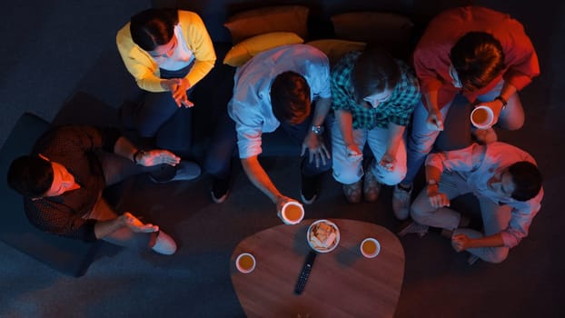 Happy family and colleague sitting at dark living room with red filter while cheering football team together. Caucasian people enjoy watching tv and giving high five and clinking glasses. Convocation.