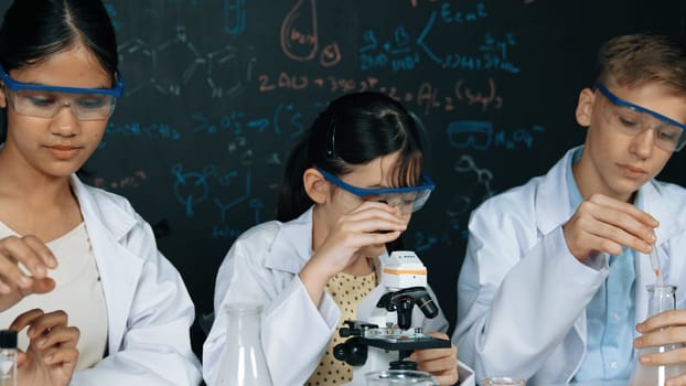Smart teenager drop sample in microscope while girl inspect carefully at blackboard with chemistry theory. Professional scientist pour chemical product in tube and prepare for experiment. Edification.