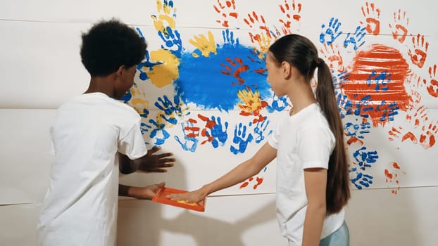 Diverse happy highschool girl and african boy paint the wall with water color in red and blue or contrast color by using their hands in art lesson. Colorful. Creative activity concept. Edification.