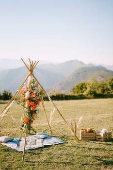 Wedding wigwam arch stands on a green meadow next to boxes of food. High quality photo