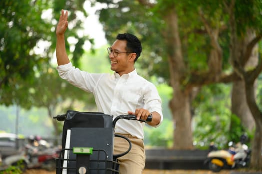 Friendly male worker riding bicycle and waving hand as greeting someone. People and transport concept.