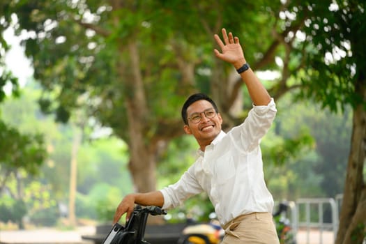 Cheerful male worker riding bicycle and waving hand as greeting someone. People and transport concept.