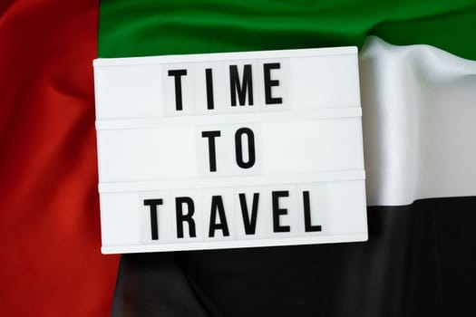 Message with text TIME TO TRAVEL on background of waving UAE flag made from silk. United Arab Emirates flag with concept of tourism and traveling. Inviting greeting card, advertisement. Dubai welcoming card