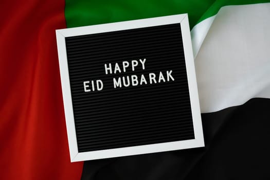 Congratulations with text HAPPY EID MUBARAK - happy holidays waving UAE flag on background concept. Greeting card advertisement. Commemoration Day Muslim Ramadan Blessed holy month public holiday. Patriotism