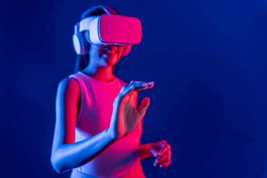 Smart female standing with surrounded by cyberpunk neon light wear VR headset connecting metaverse, futuristic cyberspace community technology. Woman using hand touching virtual object. Hallucination.