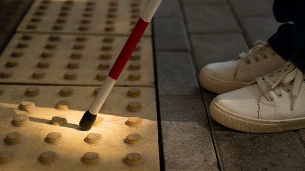 A close-up of a woman's feet with a tactile cane and a tactile tile indicating an obstacle