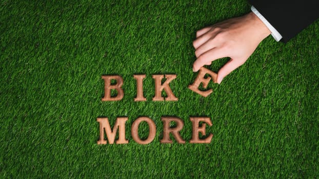 Hand arrange wooden alphabet text in BIKE MORE on green biophilic grass design background as eco symbol for encouraging message for biking campaign and environmental awareness. Gyre