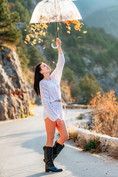 woman umbrella leaves , She holds him over her head, autumn leaves are falling out of him. Beautiful woman in a dress with an umbrella in the autumn park on the road in the mountains