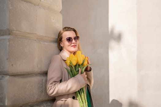 Woman holding yellow tulips, leaning against stone wall. Women's holiday concept, giving flowers