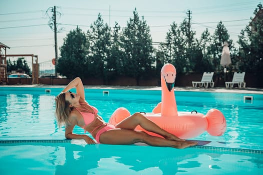 A woman is laying on a pink inflatable flamingo in a pool. The scene is bright and cheerful, with the pink flamingo adding a playful touch to the image