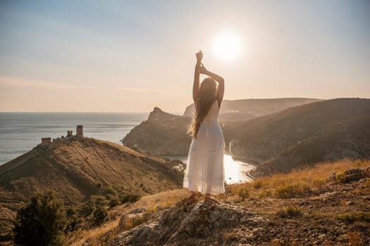 woman stands on a hill overlooking the ocean, her arms raised in the air. Concept of freedom and joy, as if the woman is celebrating a moment of happiness or accomplishment