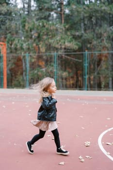 Little girl with flying hair walks along the sports field. Side view. High quality photo