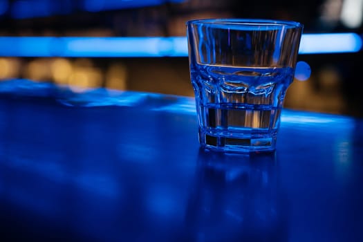 A glass of water sits on a bar counter. The bar is dimly lit, giving the scene a cozy and intimate atmosphere
