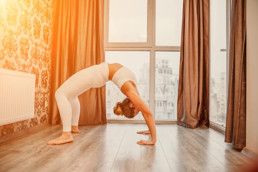 Young athletic attractive woman practicing yoga. Works out at home or in a yoga studio, sportswear, white pants and a full-length top indoors. Healthy lifestyle concept.