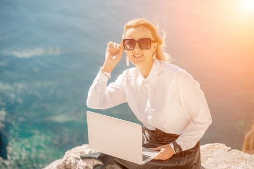 Business woman on nature in white shirt and black skirt. She works with an iPad in the open air with a beautiful view of the sea. The concept of remote work