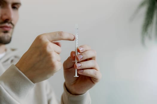 One young Caucasian handsome brunette man shakes a syringe with medicine with his fingers to get rid of air bubbles to treat his cat at home, close-up side view.