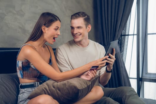 Young couple sit in the home bedroom using online payment app and digital wallet on smartphone to pay with credit card. E commerce shopping and modern purchasing via mobile internet. Unveiling