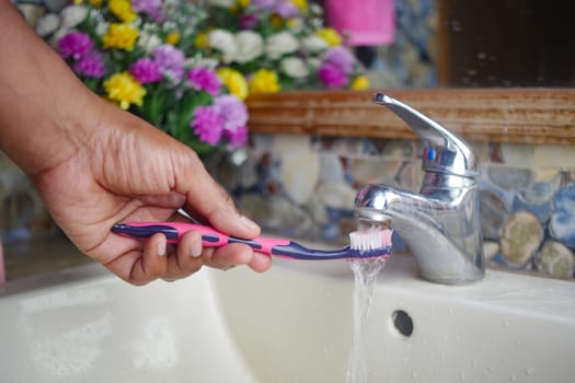 slow motion of holding toothbrush under flowing water in bathroom, closeup