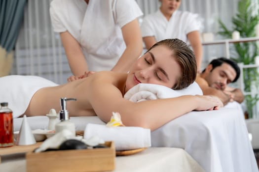 Caucasian couple customer enjoying relaxing anti-stress spa massage and pampering with beauty skin recreation leisure in day light ambient salon spa at luxury resort or hotel. Quiescent