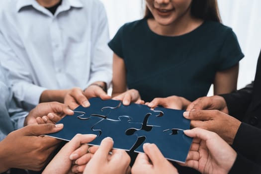 Diverse corporate officer workers collaborate in office, connecting puzzle pieces to represent partnership and teamwork. Unity and synergy in business concept by merging jigsaw puzzle. Concord