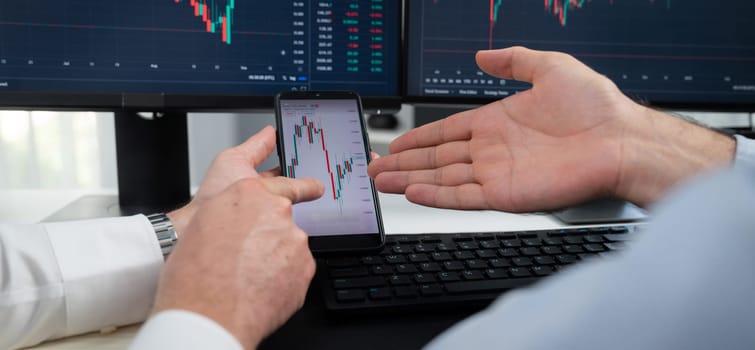 Cropped photo of exchange traders pointing lowest chart stage on dynamic graph with smartphone on panorama view, analyzing comparing with monitor and phone, discussing financial technology. Sellable.