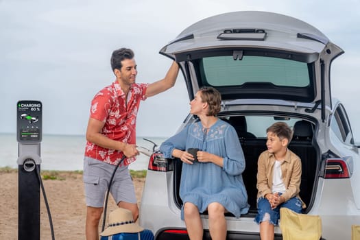 Family vacation trip traveling by the beach with electric car, happy family recharge EV car, enjoying outdoor camping coffee. Seascape travel and eco-friendly car for clean environment. Perpetual