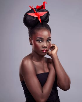 Woman, face makeup and origami in studio for beauty with red color, Oriental culture and paper bird. African model, bold cosmetics and grey background for art deco, confidence and creative design.