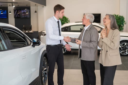 A salesman hands over the keys to a new car to an elderly Caucasian couple