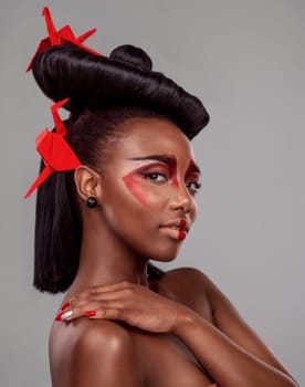 Portrait, makeup and beauty of black woman with origami in studio isolated on gray background or backdrop. Face, creative cosmetics and confident model with red paper crane in hair, skincare and art.