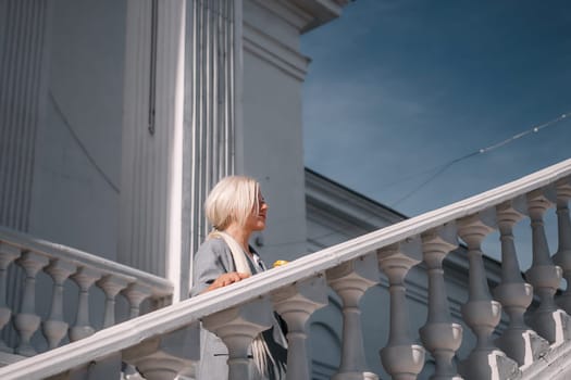 A woman is standing on a white staircase with a cup in her hand. She is smiling and looking up at the sky
