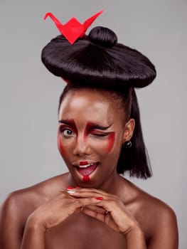 Creative beauty, wink and black woman with origami in studio isolated on dark background. Funny face, makeup and skincare with African female model, traditional and Japanese paper for art deco.