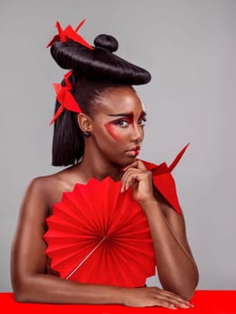 Portrait, beauty and black woman with origami for fashion, makeup and skin art in studio isolated on gray background. Face, creative cosmetics and confident model thinking of paper crane in hair.