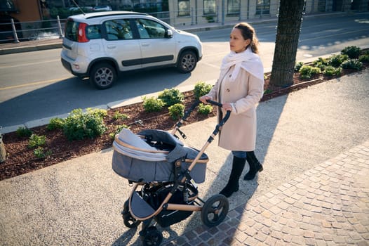 Young single mother with newborn baby in a stroller walking down the city. View from above