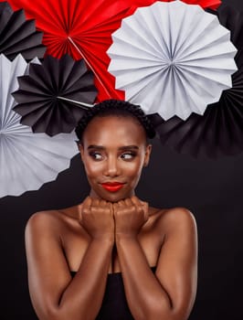 Beauty, thinking and black woman with origami fans in studio, smile and dark background. Face, makeup and cosmetics of female model with pride, traditional Japanese and paper art for culture hat.