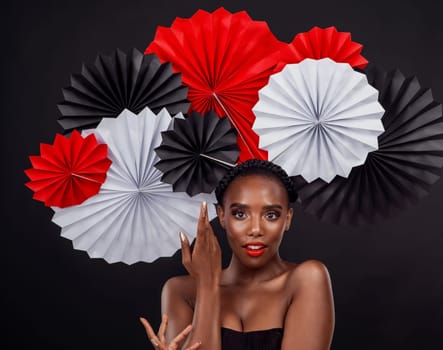 Origami fans, portrait and a African woman with art deco for culture by dark background. Creative makeup, beauty and Female model with Japanese, traditional and paper or craft on a studio backdrop.