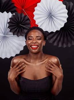 Beauty, calm and black woman with origami fans in studio, smile and dark background. Face, makeup and cosmetics of female model with pride, traditional Japanese and paper art for culture hat.